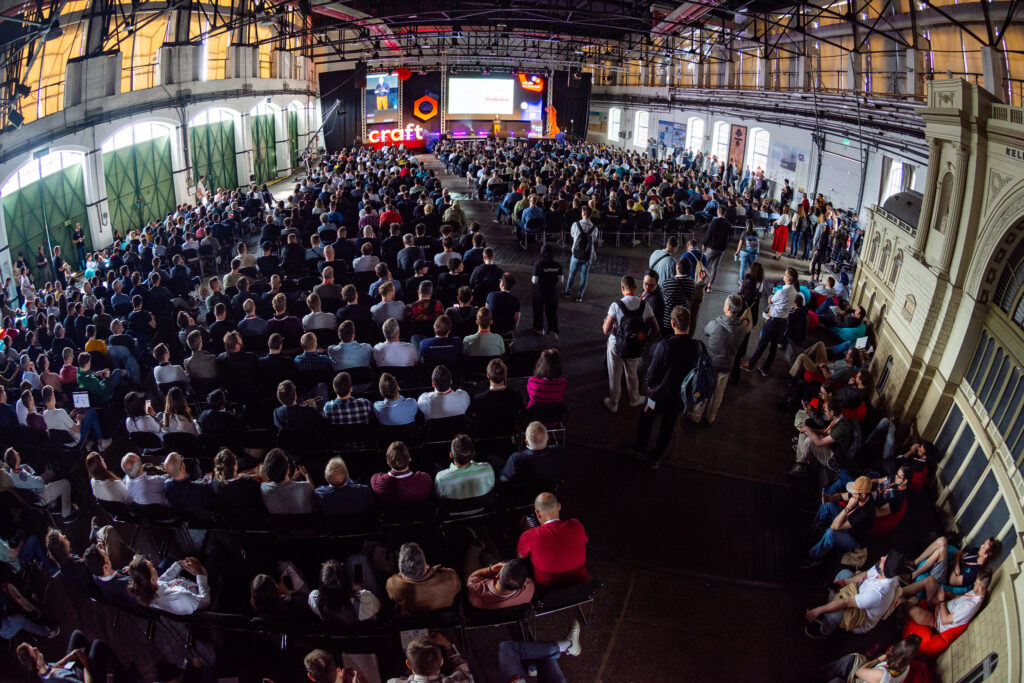 Large audience attending a keynote session at Craft Conference in a spacious industrial venue with stage and big screen